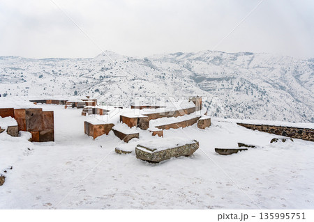 Snow-covered stone ruins stand near the Garni Temple, broken walls and ancient blocks contrast with the wide winter mountain landscape Snow-covered stone ruins stand near the Garni Temple, broken walls and ancient blocks contrast with the wide winter mountain landscape 135995751