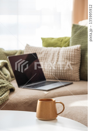Laptop on Sofa and Coffee Mug on Table. Cozy Spring Home Workspace 135995912