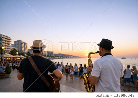 Two men, a guitarist and a saxophonist, performing street music for an audience at sunset. Live entertainment and busking concept 135996348