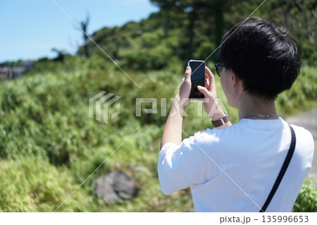 初島の風景をスマホで撮影する20代男性の後ろ姿 初島の風景をスマホで撮影する20代男性の後ろ姿 135996653