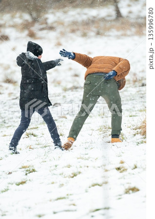 Two children playfully throw snowballs at each other during a winter snowfall. 135996780