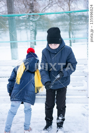 Two children play in the snow, one carefully crafting a snowball while the other watches. Two children play in the snow, one carefully crafting a snowball while the other watches. 135996824