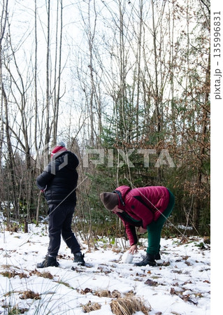 Children building a small snowman together in a snowy forest. Winter fun and outdoor activities. Children building a small snowman together in a snowy forest. Winter fun and outdoor activities. 135996831