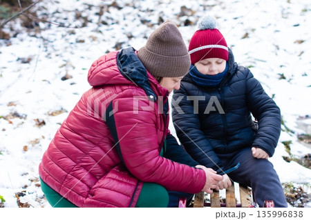 A parent and child bundled in winter wear look at a phone together outdoors in the snow. A parent and child bundled in winter wear look at a phone together outdoors in the snow. 135996838