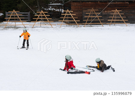 Joyful moments of children learning to ski in a snowy landscape surrounded by wooden ski racks on a crisp winter day 135996879