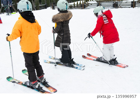 Children enjoy skiing on a snowy slope wearing colorful winter gear while experiencing the thrill of winter sports in a cheerful ski resort setting Children enjoy skiing on a snowy slope wearing colorful winter gear while experiencing the thrill of winter sports in a cheerful ski resort setting 135996957