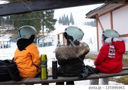 Friends admire the snowy slopes while wearing helmets, preparing for a thrilling day of skiing at a winter resort in the early morning Friends admire the snowy slopes while wearing helmets, preparing for a thrilling day of skiing at a winter resort in the early morning 135996961