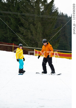 Joyful moments of snowboarding lessons in a winter wonderland with children learning and having fun on a snowy slope surrounded by lush pine trees 135996989