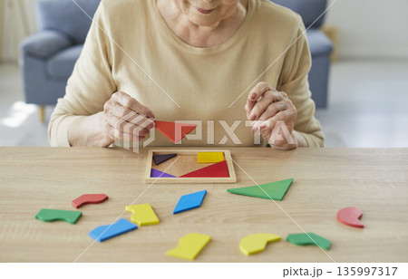 Elderly woman solving geometric puzzle for dementia therapy and brain training Elderly woman solving geometric puzzle for dementia therapy and brain training 135997317