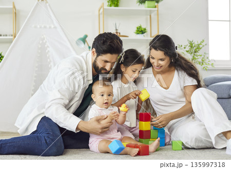 Happy parents and kids playing with colorful building blocks in living room at home Happy parents and kids playing with colorful building blocks in living room at home 135997318
