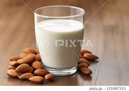 Almond Milk in Glass with Scattered Almonds on Table 135997335