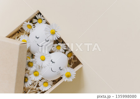 Cute Eggs with daisy flowers in a box on a yellow pastel background. Easter background. Cute Eggs with daisy flowers in a box on a yellow pastel background. Easter background. 135998080