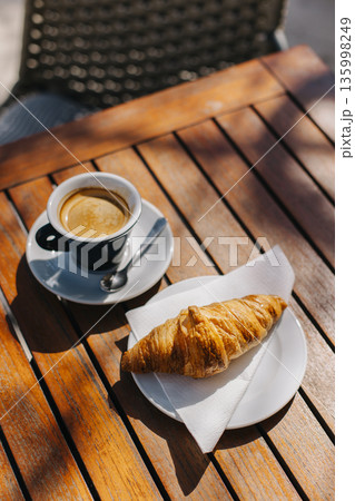 Cup of black coffee and a croissant on a table in a street cafe. 135998249