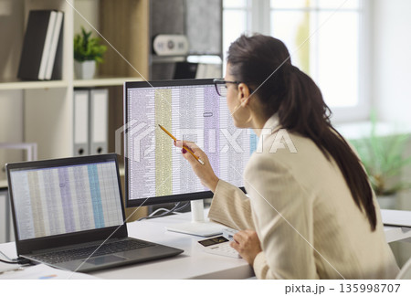 Female accountant analyzing spreadsheet data on computer monitors in modern office Female accountant analyzing spreadsheet data on computer monitors in modern office 135998707