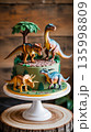 Dinosaur cake on a white stand with colorful decorations and figures in a rustic setting 135998809