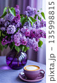 Purple flowers in a vase beside a cup of coffee on a table near a window during the day 135998815