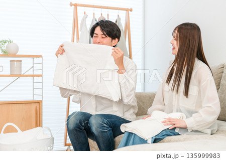 リビングで洗濯物を畳む笑顔の夫婦,カップル リビングで洗濯物を畳む笑顔の夫婦,カップル 135999983