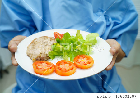 Asian elderly woman patient eating pork chop stake and vegetable salad for healthy food in hospital. Asian elderly woman patient eating pork chop stake and vegetable salad for healthy food in hospital. 136002307