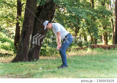 ゴルフコースで林の中からトラブルショットを打つ男性ゴルファー 136003829