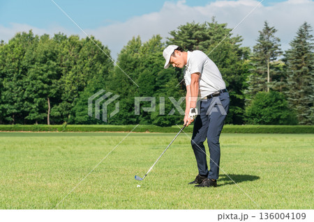 ゴルフ場でゴルフをするゴルファーの男性（アイアンショット） 136004109