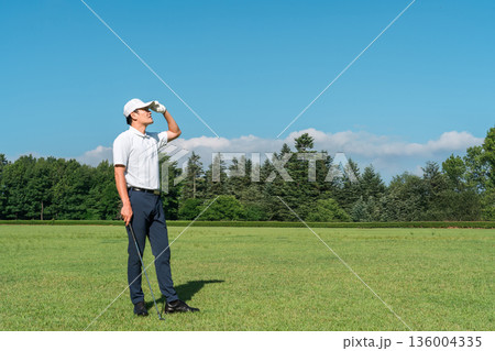 新緑の中でゴルフウェアを着た男性ゴルファー（ゴルフコース・アカデミー・会員権） 136004335