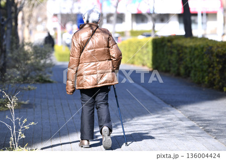 日本の横浜都市景観光と“陰”…高齢化社会　杖の高齢女性（マスク姿）。体が右に傾く…左手は寒そうに… 136004424