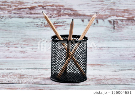 Three freshly sharpened wooden pencils are neatly arranged within a cylindrical black metal mesh holder 136004681