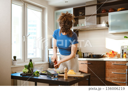 Woman sprinkles pepper over smashed broccoli with cheese in a kitchen during daytime preparation 136006219