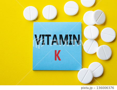Vitamin K symbol. Concept word Vitamin K on blue note. Beautiful yellow background with pills. Medicine and Vitamin K concept. Copy space 136006376