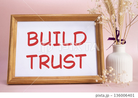 Build trust symbol. Concept words Build trust on beautiful wooden picture frame. Beautiful pink background with flower vase. Business and Build trust concept. Copy space. Build trust symbol. Concept words Build trust on beautiful wooden picture frame. Beautiful pink background with flower vase. Business and Build trust concept. Copy space. 136006401