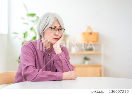 マイホームのダイニングテーブルに座り考え事をするシルバーヘアのシニア女性 136007239