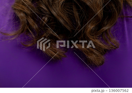 Detailed studio image featuring wavy brown hair and purple cloth, Intimate studio portrait capturing glossy wavy brown hair draped over purple fabric background 136007562