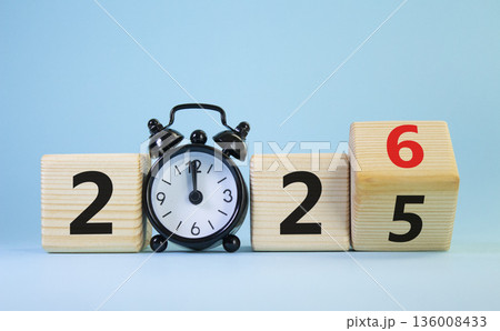 2026 New Year symbol. Businessman turns wooden cube and changes Year 2025 to 2026. Beautiful light blue background with Alarm clock. Copy space. Business and 2026 happy new year concept 136008433