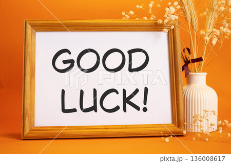 Good luck symbol. Concept words Good luck on beautiful wooden picture frame. Beautiful orange background with flower vase. Business and Good luck concept. Copy space. Good luck symbol. Concept words Good luck on beautiful wooden picture frame. Beautiful orange background with flower vase. Business and Good luck concept. Copy space. 136008617