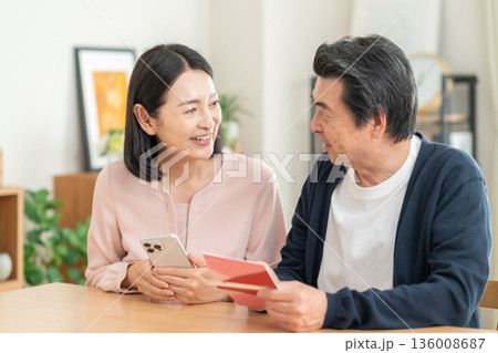 リビングで貯金通帳を見るミドルの夫婦 136008687
