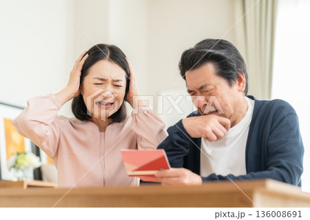 リビングで貯金通帳を見るミドルの夫婦 リビングで貯金通帳を見るミドルの夫婦 136008691