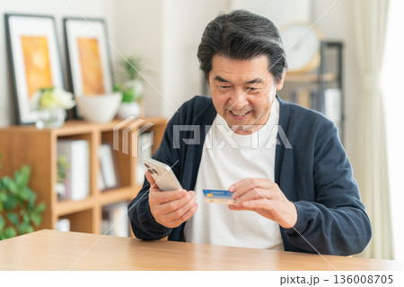 リビングでクレジットカートとスマホを見るミドルの男性 リビングでクレジットカートとスマホを見るミドルの男性 136008705