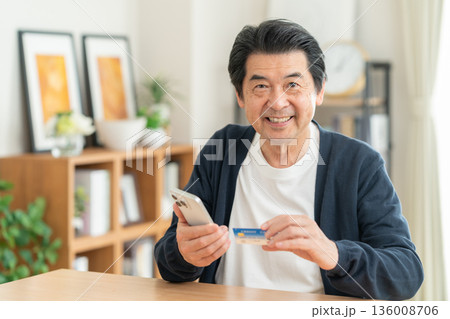 リビングでクレジットカートとスマホを見るミドルの男性 リビングでクレジットカートとスマホを見るミドルの男性 136008706