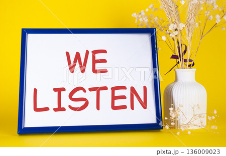 We listen symbol. Concept words We listen on beautiful wooden picture frame. Beautiful yellow background with flower vase. Business and We listen concept. Copy space. 136009023