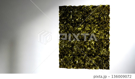 Japanese minimalist.a suspended nori seaweed sheet backlit by soft window light, revealing its delicate perforated structure and crisp edges, against a plain white wall  136009072