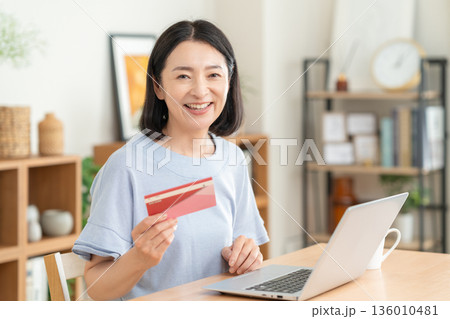 リビングで貯金通帳を見るミドルの女性 136010481