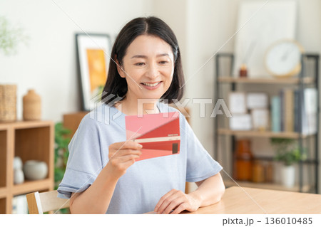 リビングで貯金通帳を見るミドルの女性 136010485