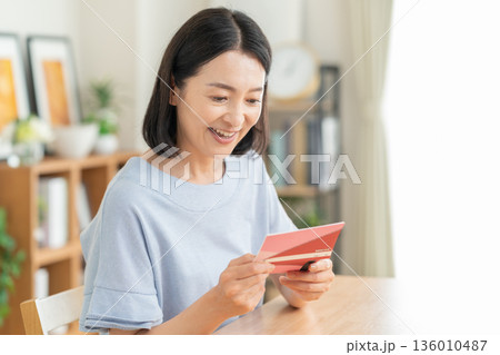 リビングで貯金通帳を見るミドルの女性 136010487