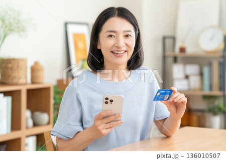 リビングでクレジットカートとスマホを見るミドルの女性 リビングでクレジットカートとスマホを見るミドルの女性 136010507