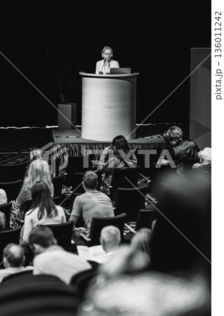Female speaker giving a talk on corporate business conference. Unrecognizable people in audience at conference hall. Business and Entrepreneurship event 136011242
