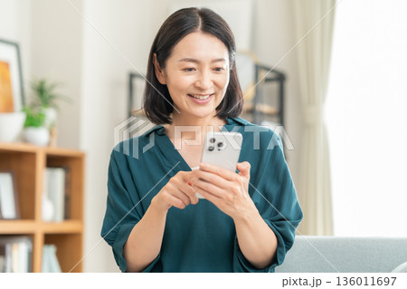 リビングでスマホを見るミドルの女性 リビングでスマホを見るミドルの女性 136011697