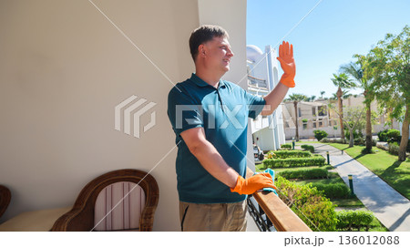 Happy Man on His Balcony Joyfully Greeting Neighbors, Embracing Community Spirit and Connection in a Bright, Welcoming Home Environment 136012088