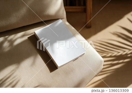 book cover mockup design. blank book template on soft beige armchair in living room or hotel room, shadow overlay 136013309
