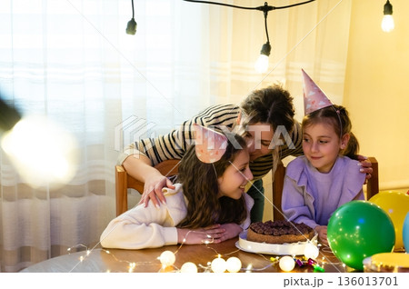 Celebrating a birthday with laughter, cake, and party hats indoors during a cozy evening gathering filled with lights and joy 136013701