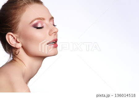 Closeup woman face with glitter eyeshadow and dewy makeup, soft studio lighting, gold hoop earring, hair swept back, serene expression, beauty commercial mood, smooth skin texture 136014518